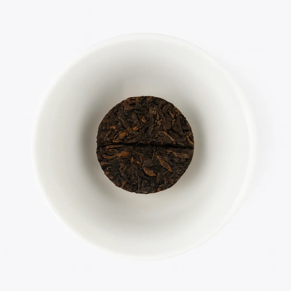 Round dark brown tea cake on a white plate with a white background