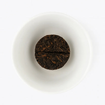 Round dark brown tea cake on a white plate with a white background